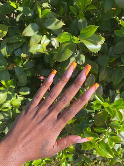 A queer black woman's hand showing of her nail art in orange in red