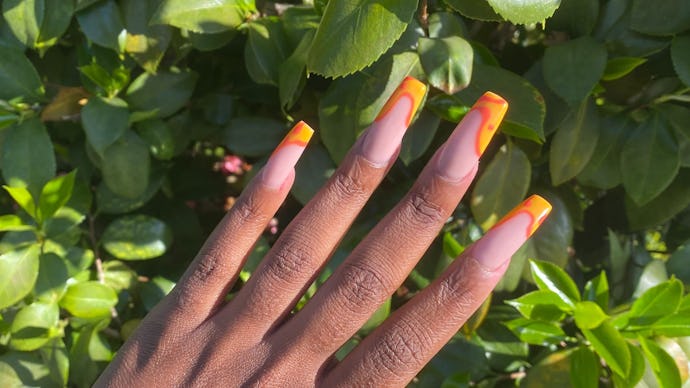 A queer black woman's hand showing of her nail art in orange in red