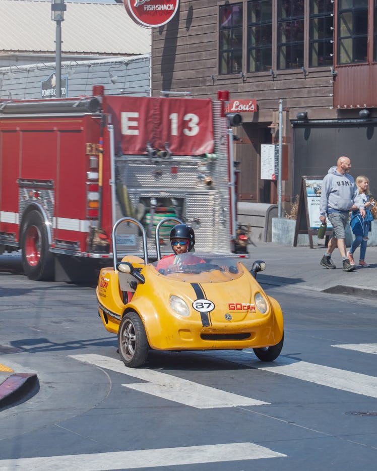 Toro y Moi in a yellow go-kart driving down a street