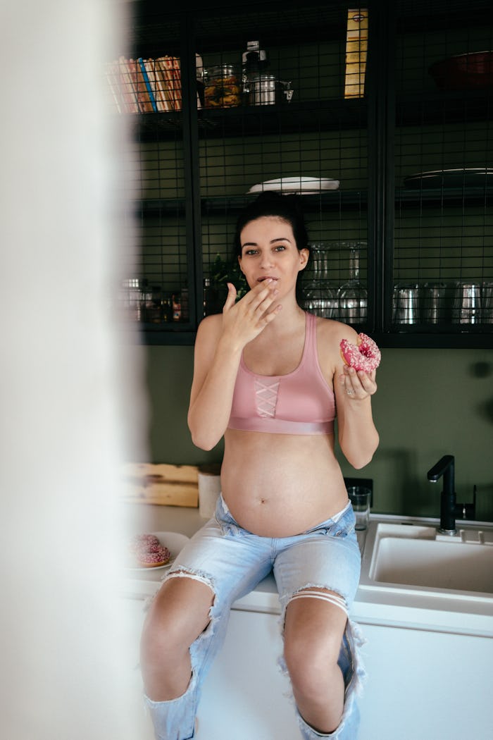 Pregnant woman on a counter eating what she's craving: a donut!