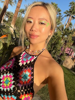 A blonde woman wearing a colorful crochet top with palms in her background