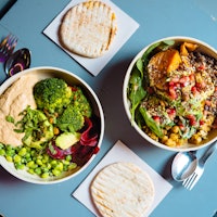 Bowls of plant-based meals on a table with pita bread