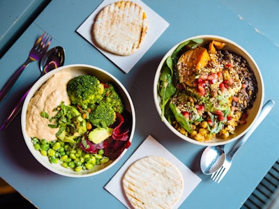 Bowls of plant-based meals on a table with pita bread