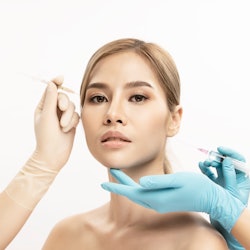 woman with cheek filler needle and glove hands