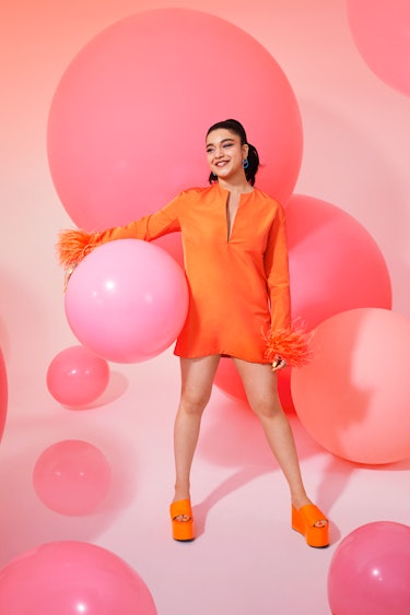 Iman Vellani posing in an orange Valentino dress next to pink balloons 
