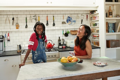 Young women laughing in the kitchen of their first apartment.