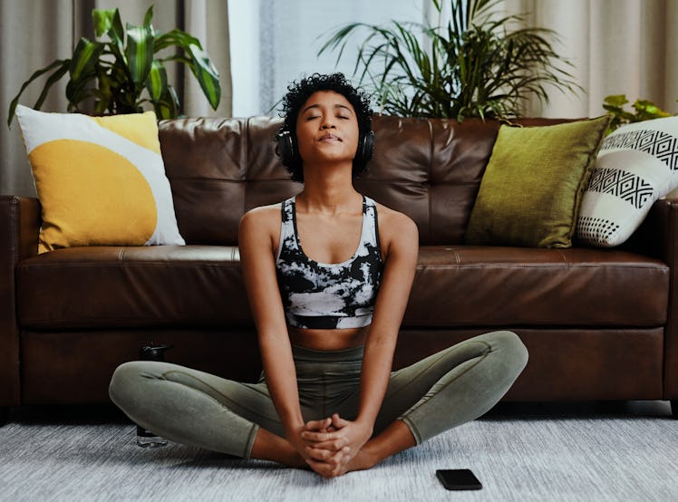 Young woman meditating in her living room after splurging and saving on her first apartment.