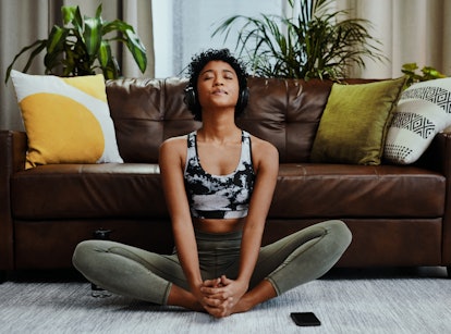 Young woman meditating in her living room after splurging and saving on her first apartment.