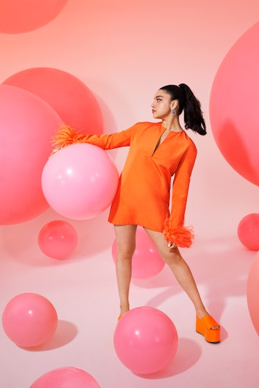 Iman Vellani standing in an orange Valentino dress and holding a big pink ball
