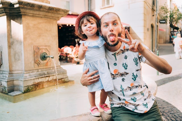 A cool little girl and her father pose in front of a fountain.