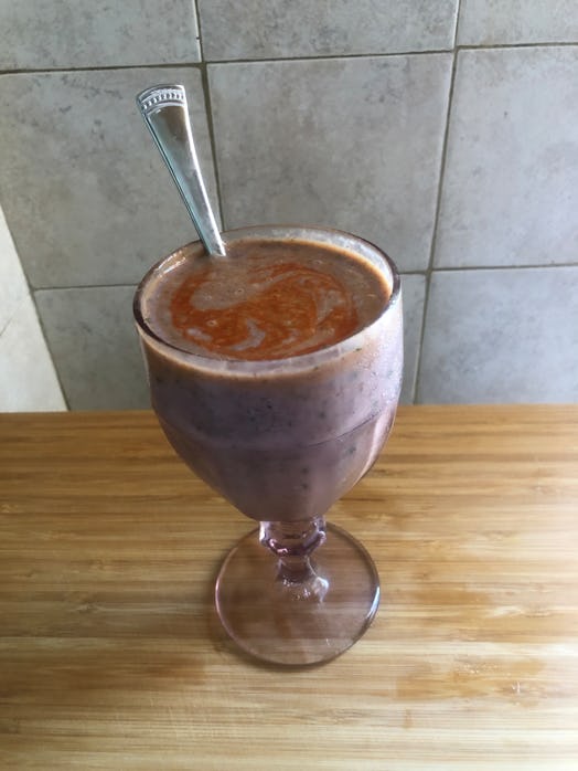 A glass of smoothie with liquid on top and a spoon sticking out
