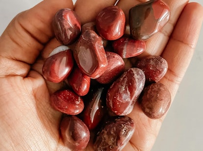 Close up of a palm full of tumbled red jasper stones, a root chakra crystal