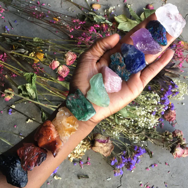 Woman's hand holding a line up of eleven different colored crystals for the chakras above a spread o...