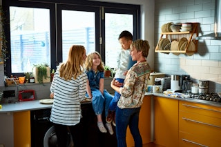 Little girl sitting on a kitchen counter and talking with her mum and adoptive parents