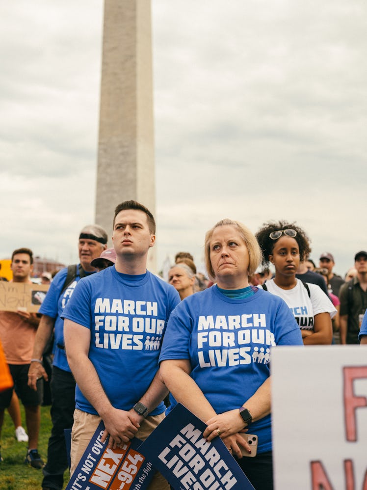 Two protestors standing near the Washington Monument, wearing blue March for Our Lives t-shirts, lis...