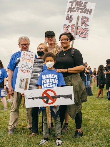 A multi-generational family of protestors stands with their handmade signs. One sign reads, "AR-15s ...