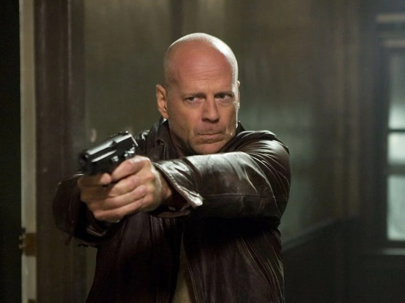 Bruce Willis aiming with the gun with a serious face while wearing a brown leather jacket
