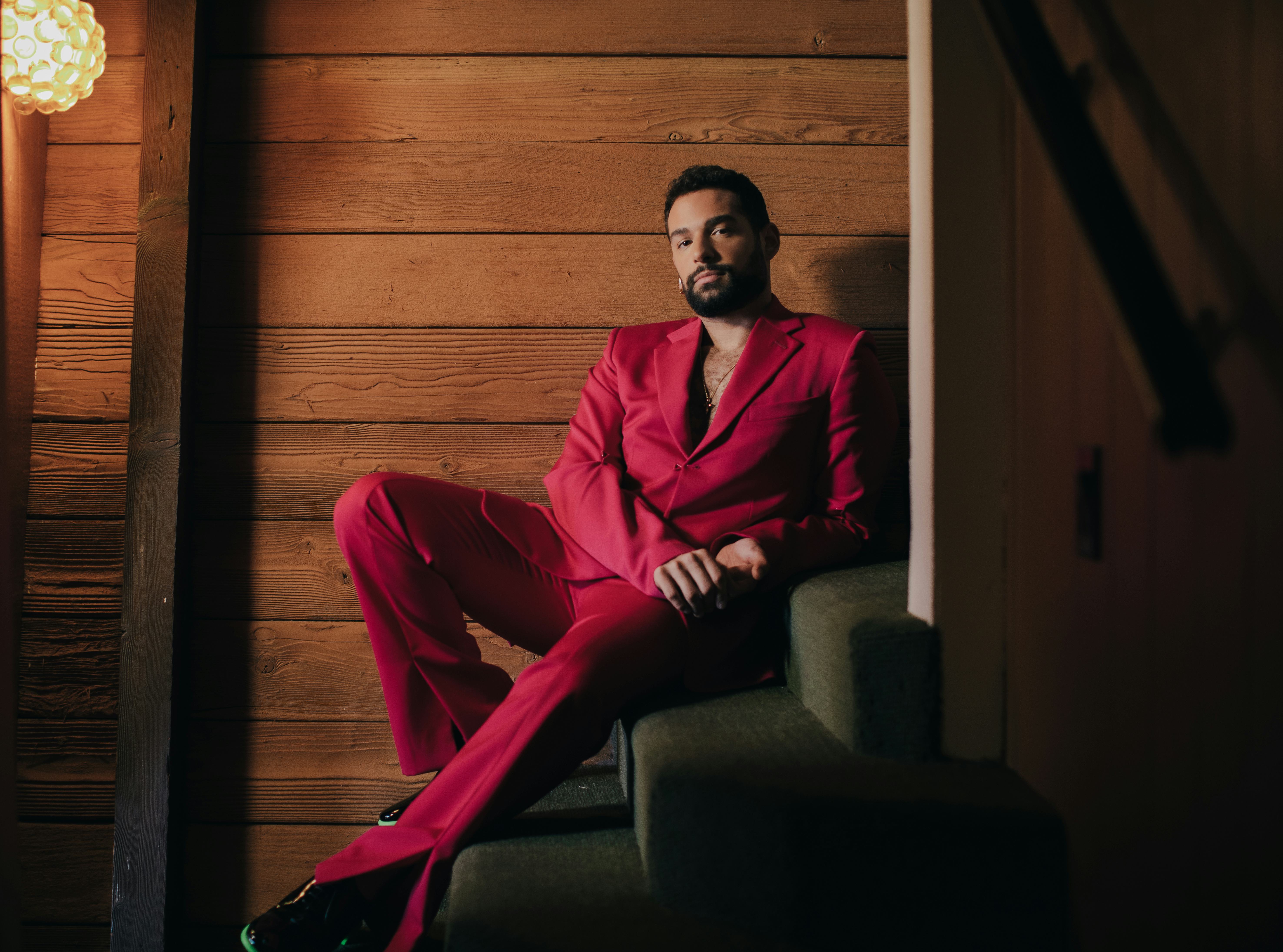 Johnny Sibilly lounging on the stairs, in a red suit