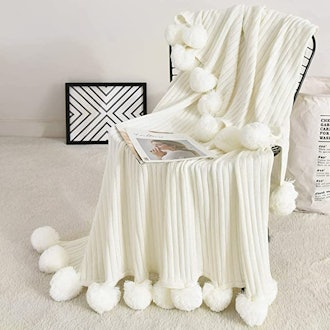 This soft cotton knit blanket has oversize pom-poms that add a comforting weight.