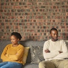 Black couple sitting on couch looking irritated at one another