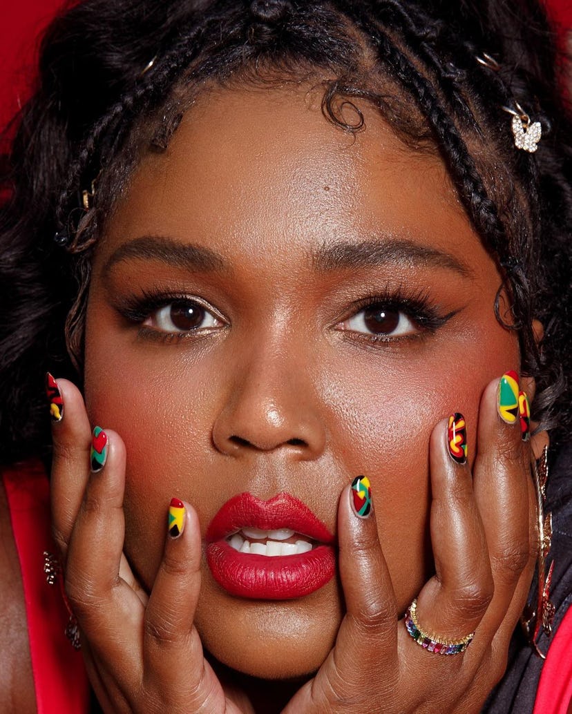 Lizzo posing with hands on side of face, nails painted in Pan African flag colors