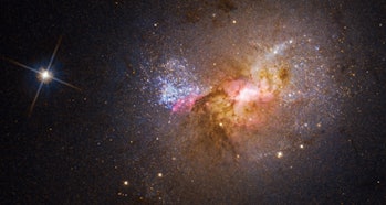 एक बौनी आकाशगंगा की हबल तस्वीर जिसमें गांगेय केंद्र से एक चमकीले तारे के रूप में बहने वाली सामग्री है ...
