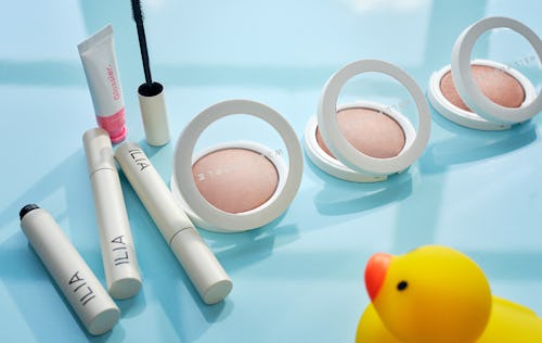 Pregnancy make up products from Ilia, Glossier and Well People placed on a blue table in front of a ...