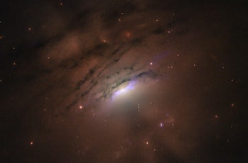 Hubble photo of brightly glowing galactic center surrounded by spiral clouds of dust and gas.