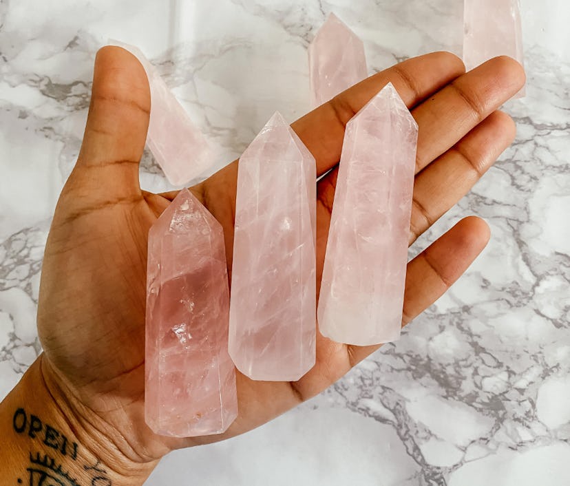 A palm face up holding three rose quartz crystal tower points, a protection crystal, over a marble b...