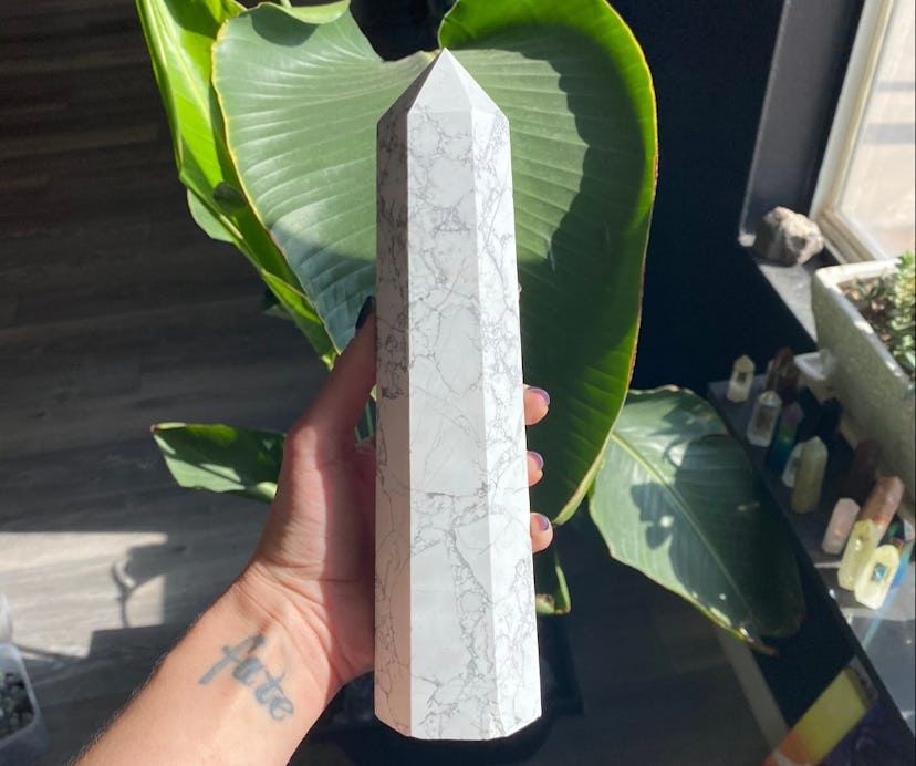 Hand holding large tower of howlite healing protective crystal in front of house plant