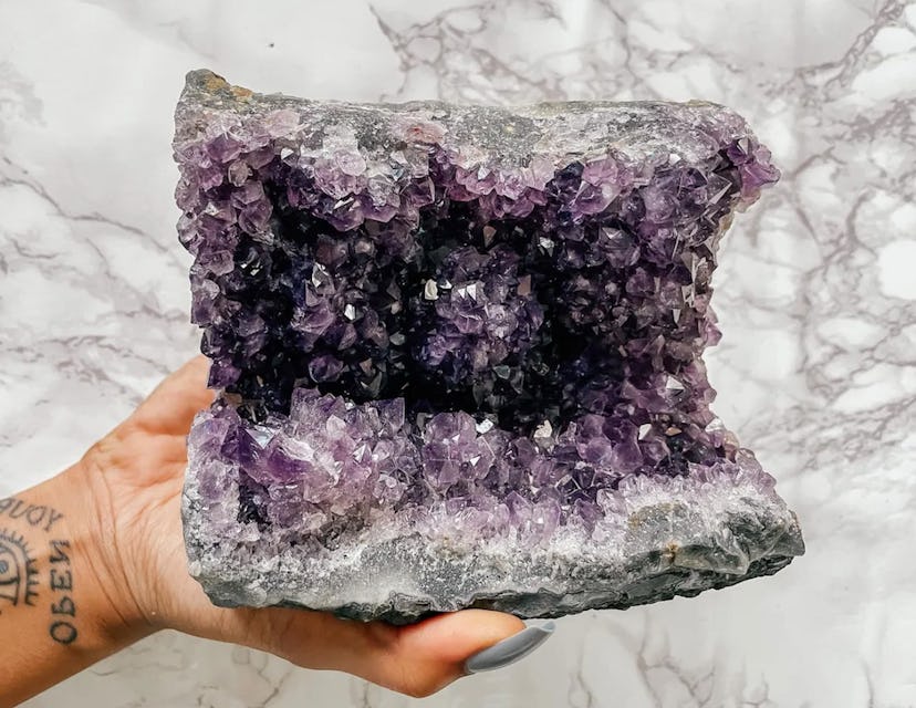 Hand holding large amethyst cluster crystal, a protection stone for the home, over a marble backgrou...