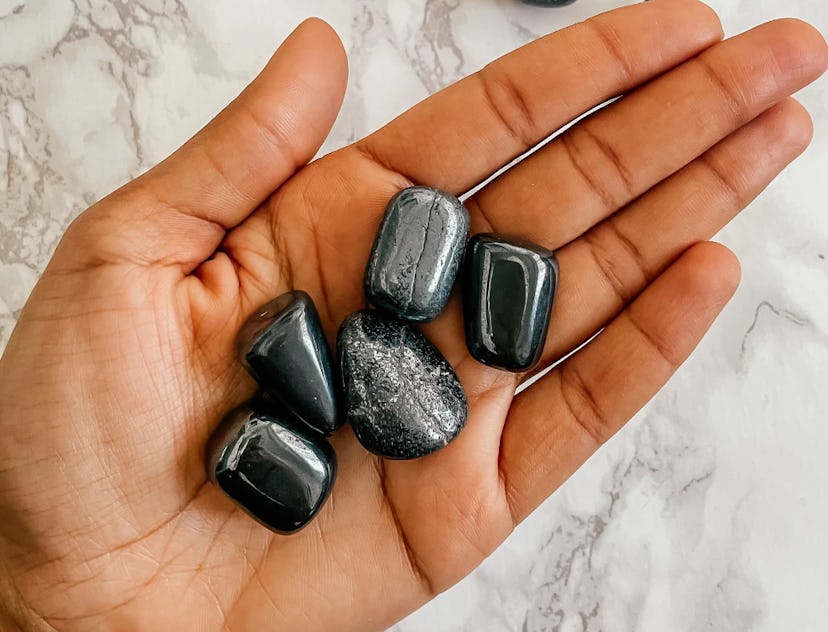 Palm face up holding five tumbled hematite stones over a marble background, a protection crystal for...