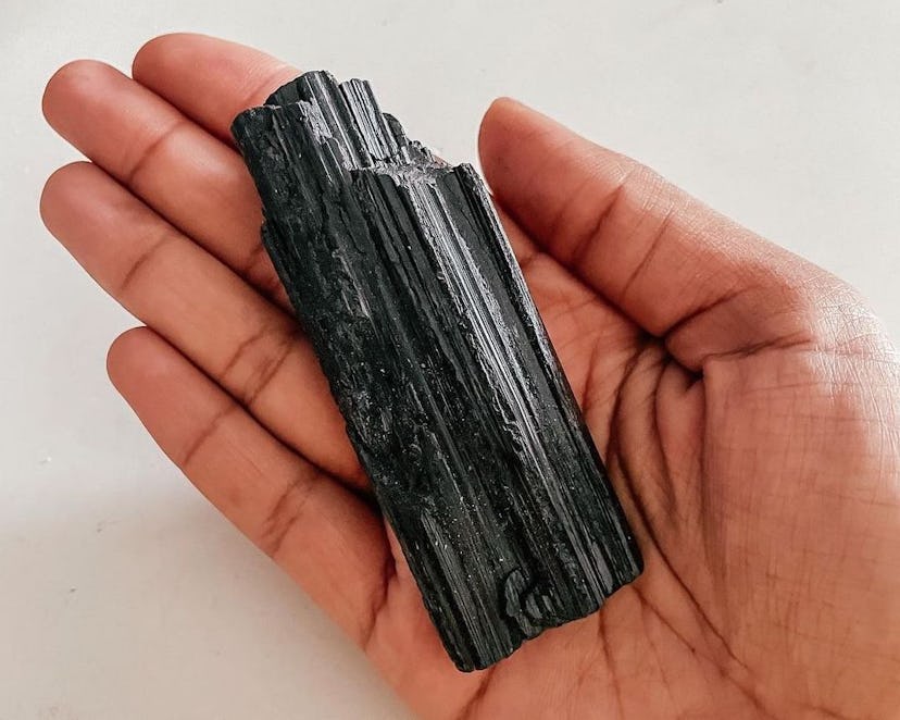 Close up of palm holding a black tourmaline stone on a white background. This is a crystal to protec...
