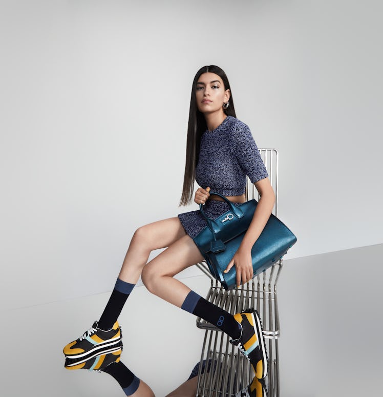 Female model in a cropped dark grey sweater and a matching mini skirt, long socks and yellow trainer...