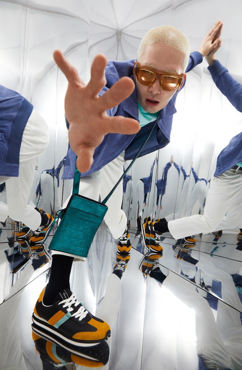 Male model with bleached hair in a blue blazer, turquoise t-shirt and white pants, sporting oversize...