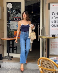 Jeanne Damas in jeans and a blue tank top carrying a wicker basket bag