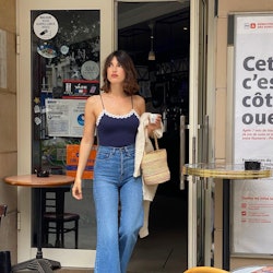 Jeanne Damas in jeans and a blue tank top carrying a wicker basket bag