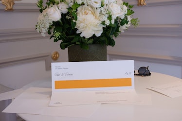 An Hermes fashion show invitation sitting on a table with some white flowers