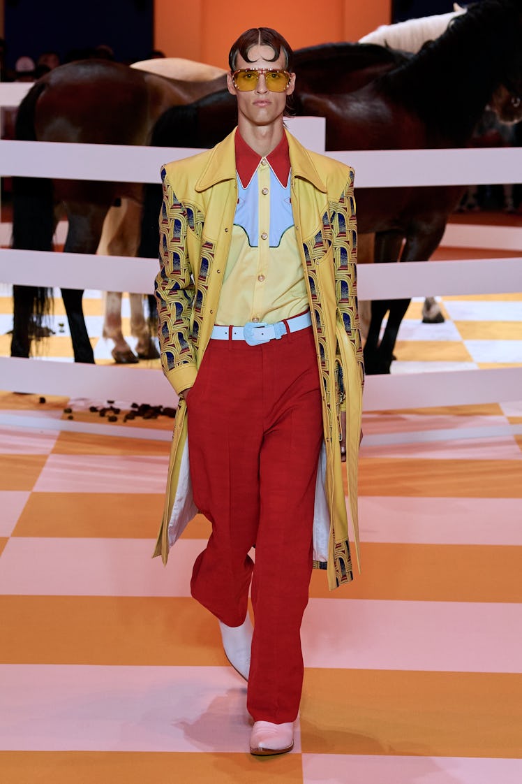 A model wearing Casablanca, with a yellow patterned coat, a button down shirt, red pants and pointed...