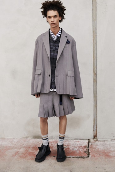 A model wearing a Sacai gray blazer, a sweater and a gray skirt