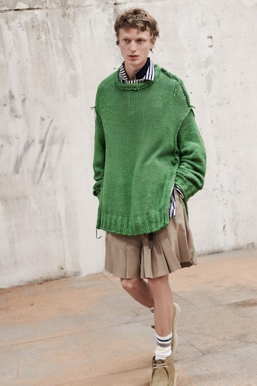 A model wearing a Sacai green oversized sweater and a beige skirt