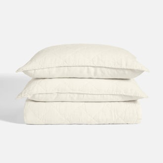 two pillows stacked atop a blanket with creme linen quilt set