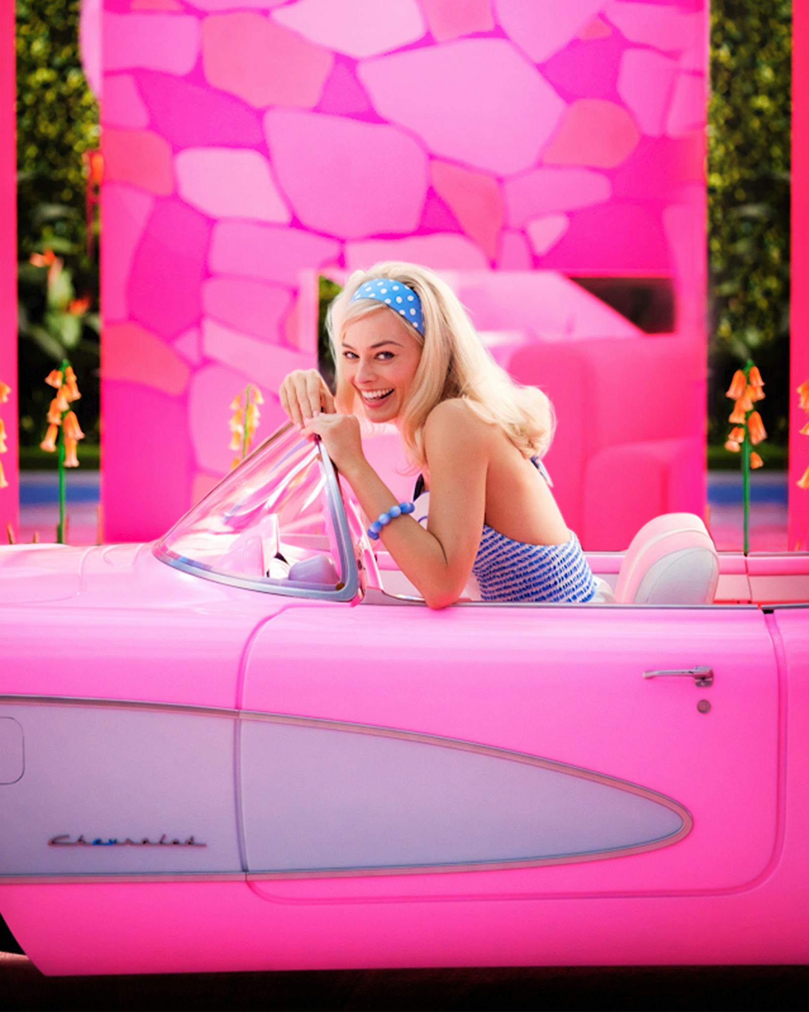 Margot Robie as Barbie in a pink convertible car.
