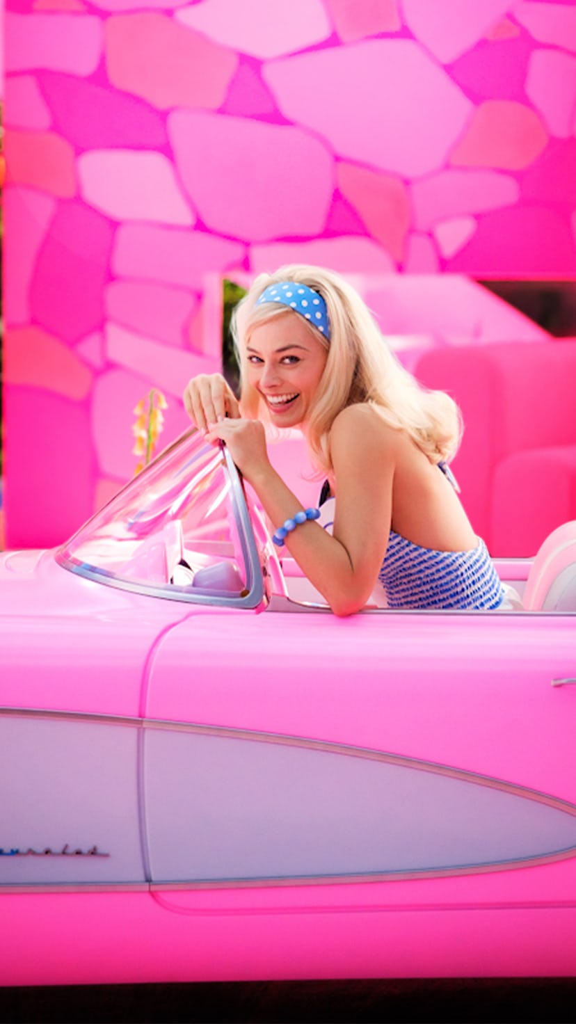 Margot Robie as Barbie in a pink convertible car.