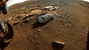 The tire of a Mars rover next to a gray streaked rock on reddish sand