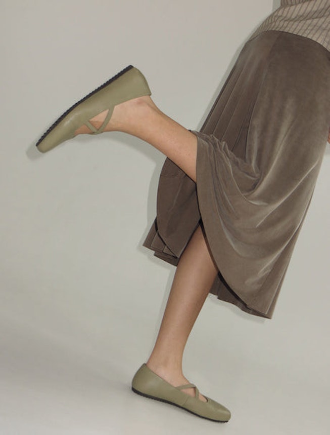 A woman wearing a light brown skirt, and khaki shirt paired with Pipa ballet flats in a light khaki