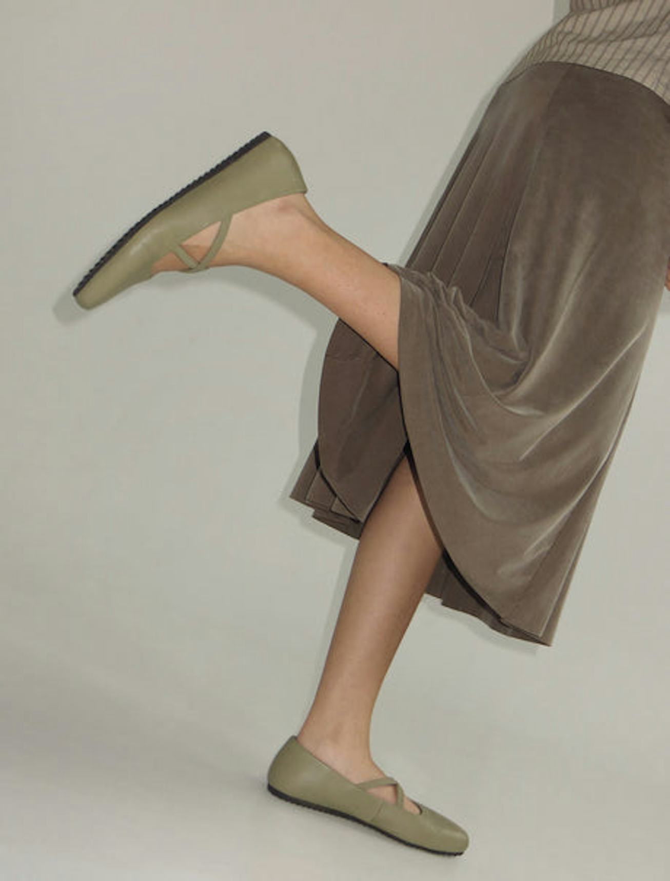 A woman wearing a light brown skirt, and khaki shirt paired with Pipa ballet flats in a light khaki