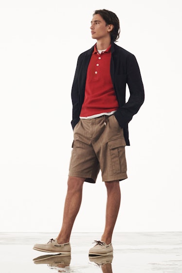 A model wearing Brunello Cucinell, a black sweater, red collared shirt and brown shorts