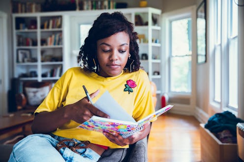A young woman sitting in a living room and doing a mental health self-assessment in her notebook