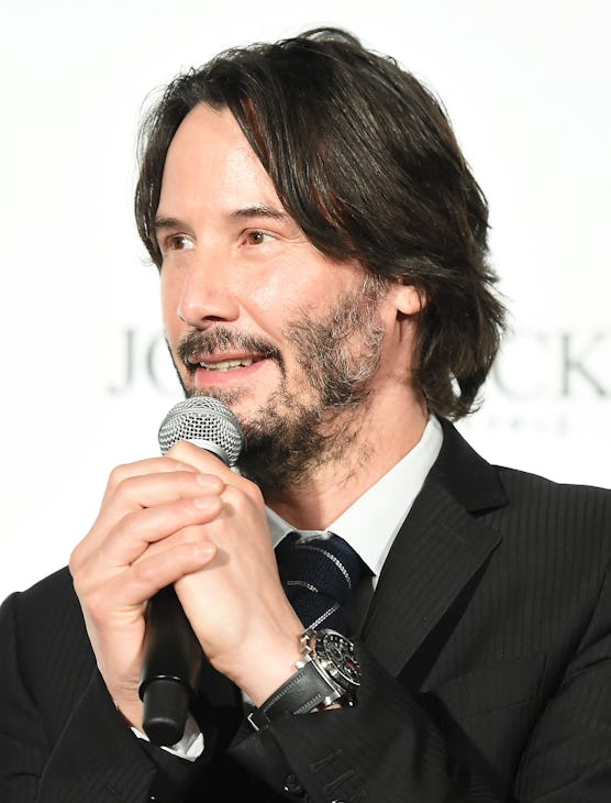 Full-profiled Keanu Reeves with patchy beard holding a microphone